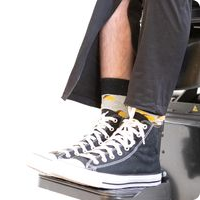 Mans feet shown wearing black converse type shoes and black jeans with zip open at the ankle